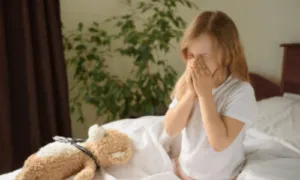 una bambina starnutisce sul letto con un peluche